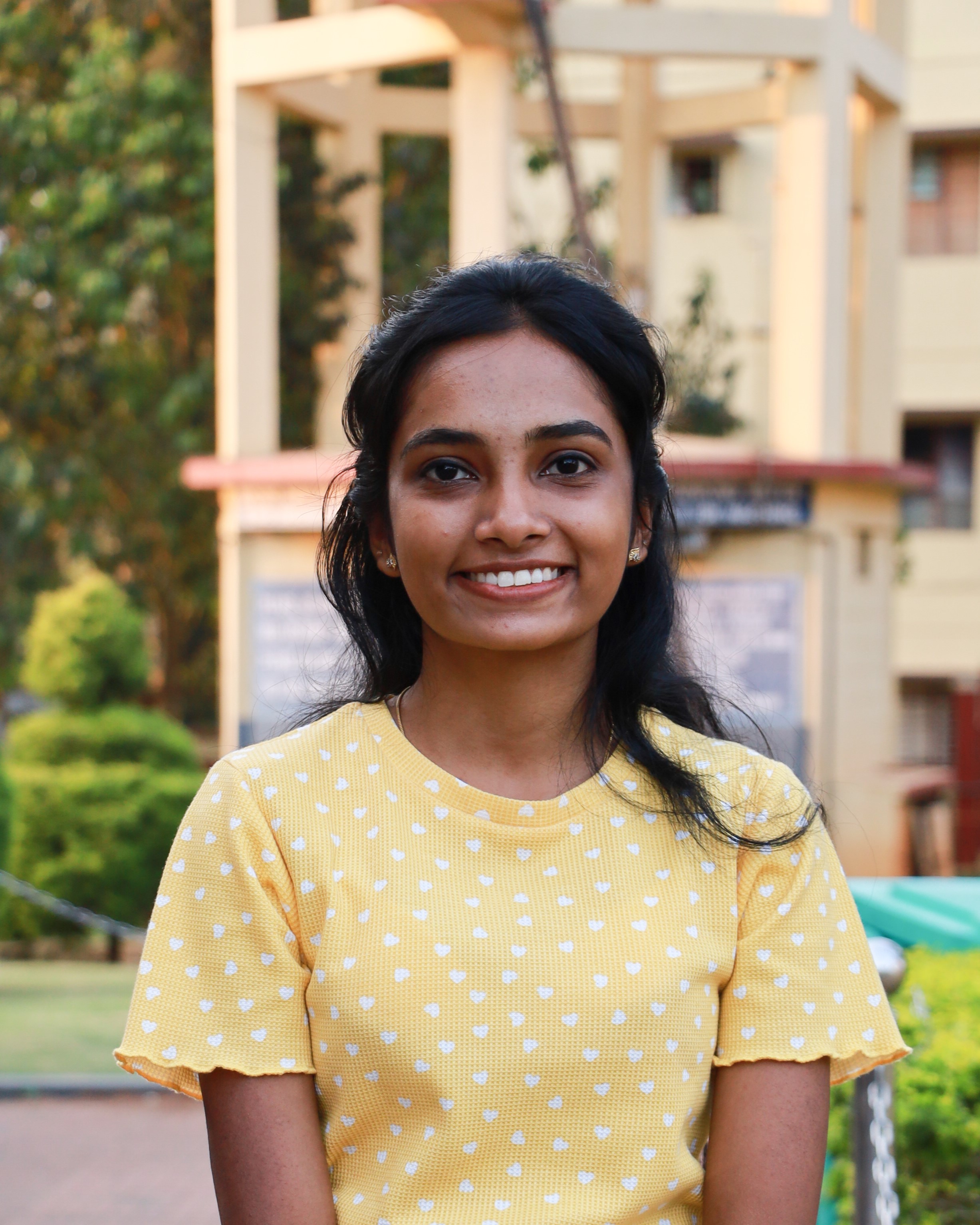 Portrait of a cheerful software developer in Kochi, Kerala,
						wearing a bright yellow top with polka dots, set against a serene outdoor backdrop