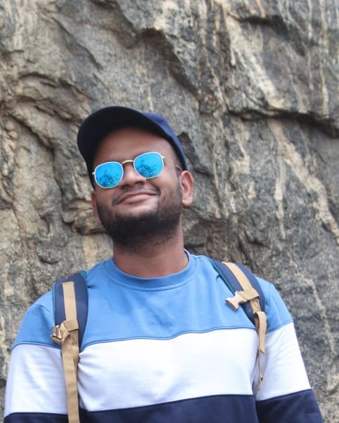 Casual portrait of a software developer in Kochi, Kerala,
						sporting sunglasses and a backpack, standing against a rugged rocky background