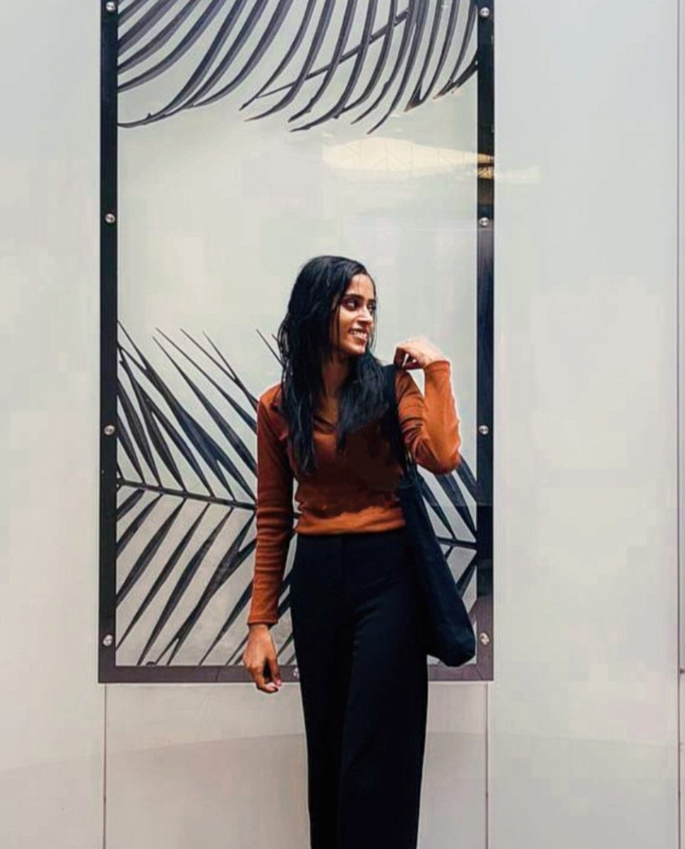 Fashion-forward software developer in Kochi, Kerala,
						standing against a modern backdrop, dressed in a chic brown top and black trousers.