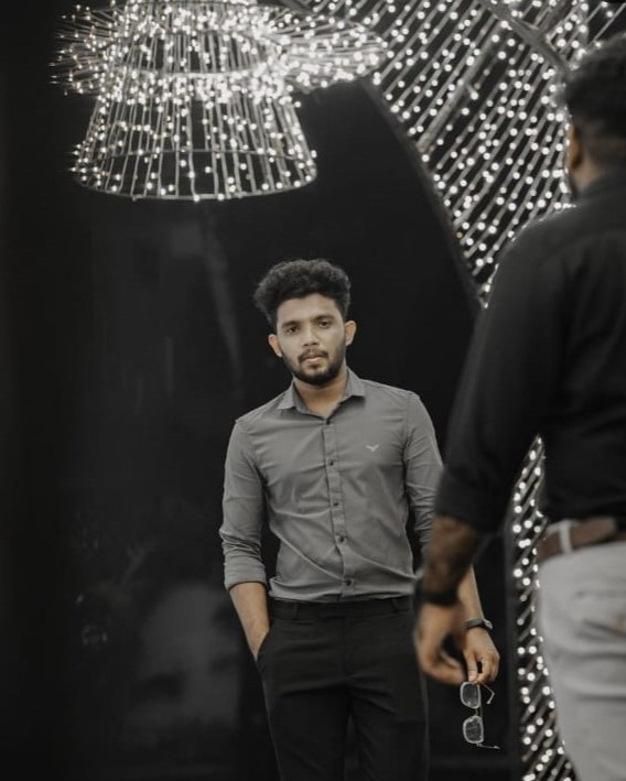 Stylish young software developer in Kochi, Kerala, dressed in a
						formal grey shirt, standing under decorative lights with a confident expression.