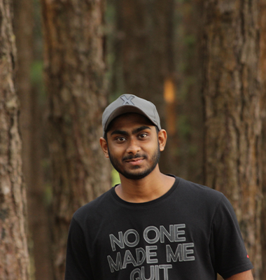 Young software developer in Kochi, Kerala, captured outdoors
						amidst lush pine trees, wearing a casual black t-shirt with a witty slogan