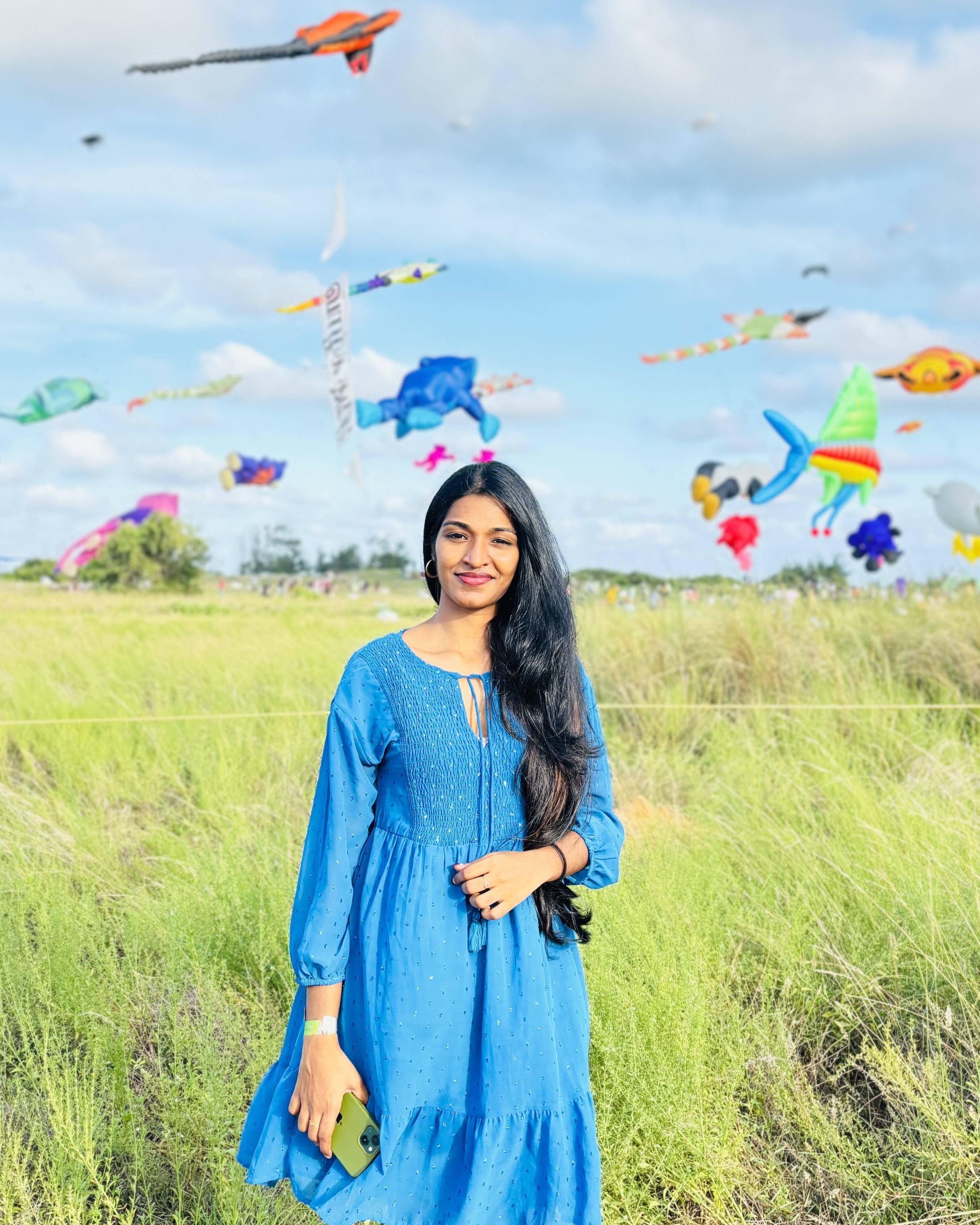 Software developer in Kochi, Kerala, wearing a vibrant blue
						dress, standing in a picturesque field with colorful kites flying in the background