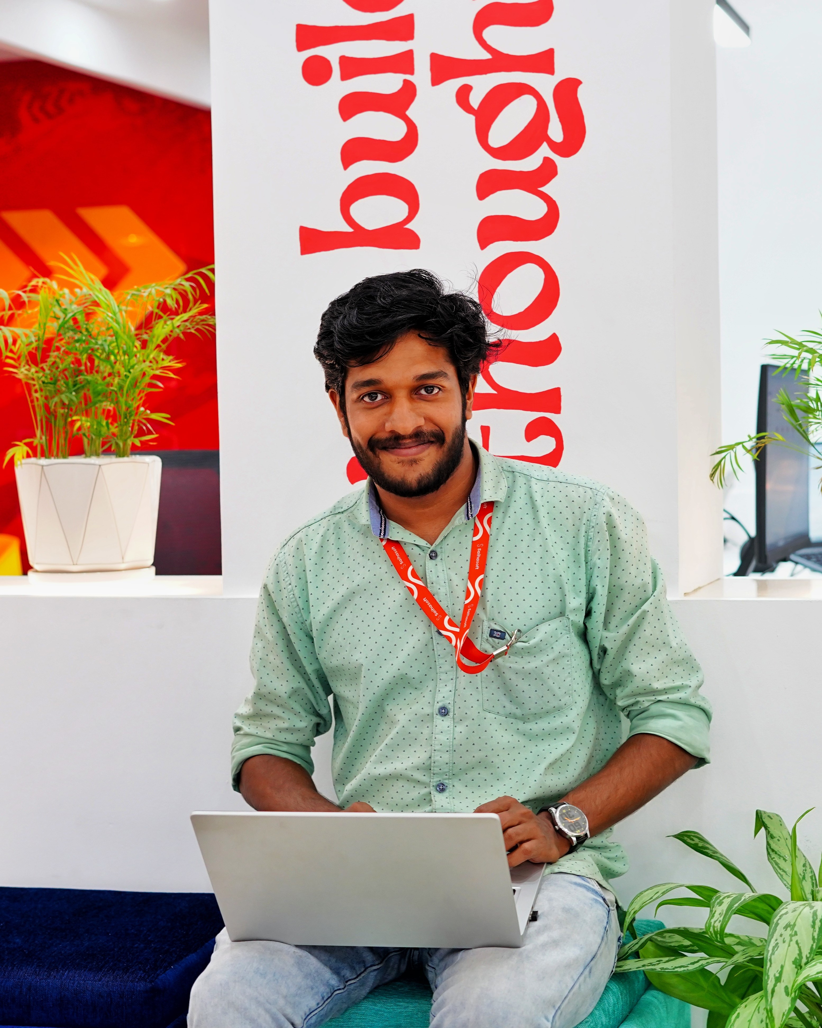 Dedicated software developer in Kochi, Kerala, working on a
						laptop in a creative workspace, wearing a mint green shirt.