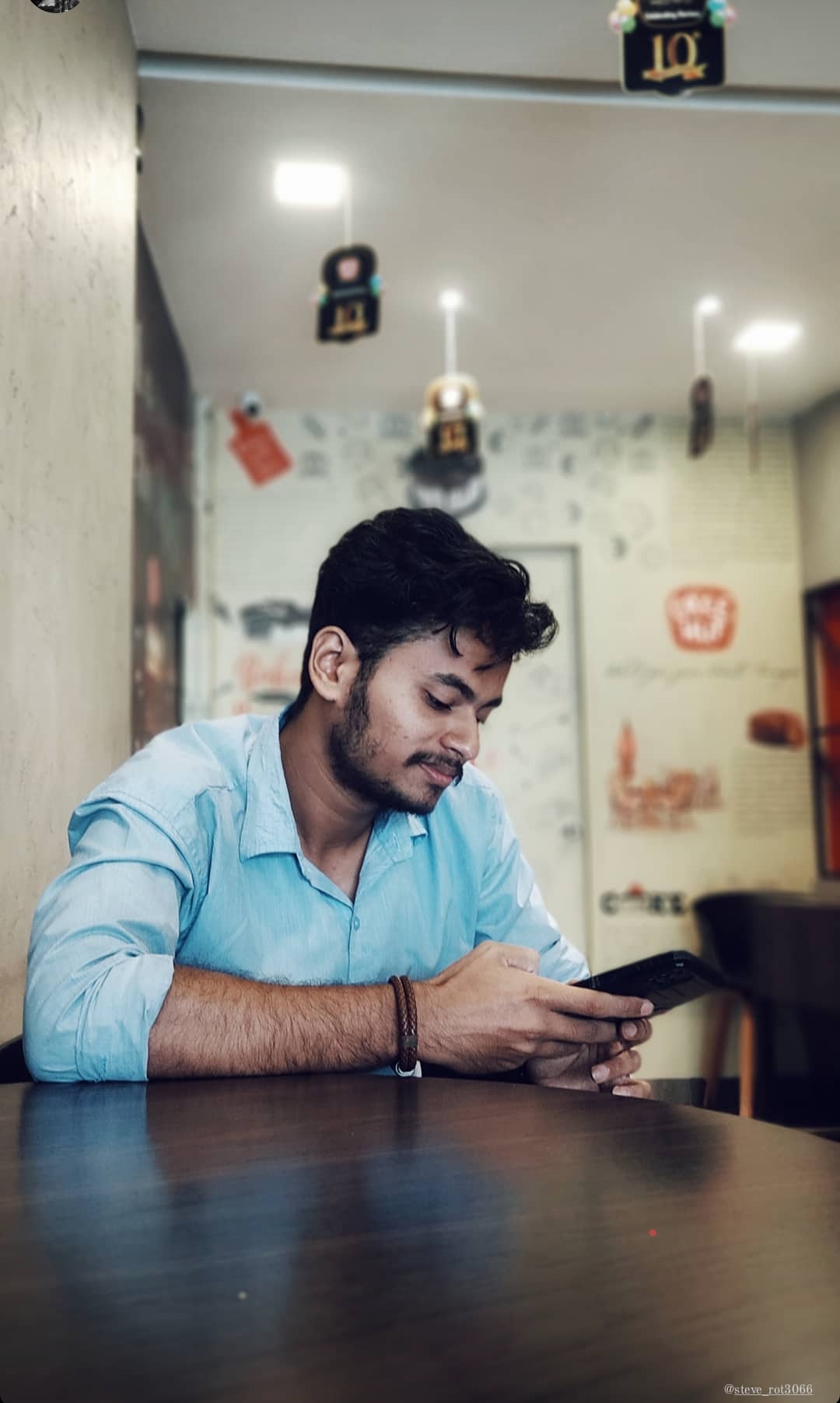 Young professional software developer in Kochi, Kerala, wearing a
						light blue shirt, working on a smartphone in a casual cafe environment.