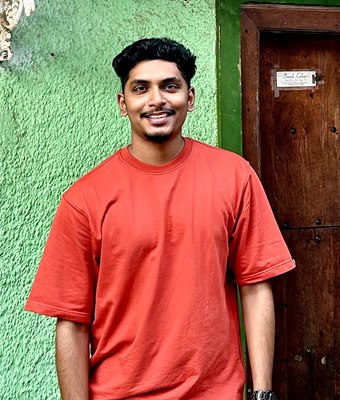 Smiling software developer in Kochi, Kerala, wearing a bright red t-shirt, standing beside an old wooden door and a green heritage wall in Fort Kochi.