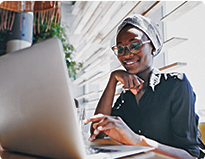 A woman wearing glasses and a head scarf is focused on her laptop, engaged in work or study.