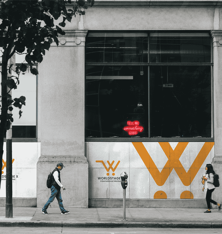 A man and woman stroll by a building featuring the yellow and white logo of WORLDSTAGE X company.